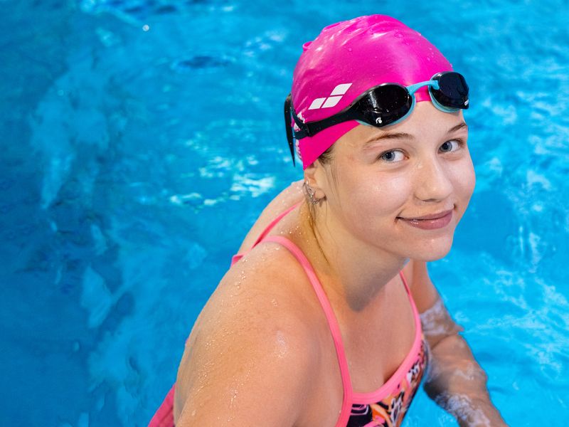Улыбающаяся девочка в розовой шапочке и купальнике у бортика, в школе плавания SPN