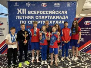 Группа спортсменов с медалями и кубком на фоне баннера всероссийской спартакиады по спорту глухих