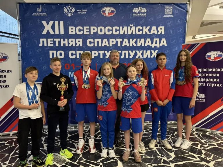 Группа спортсменов с медалями и кубком на фоне баннера всероссийской спартакиады по спорту глухих
